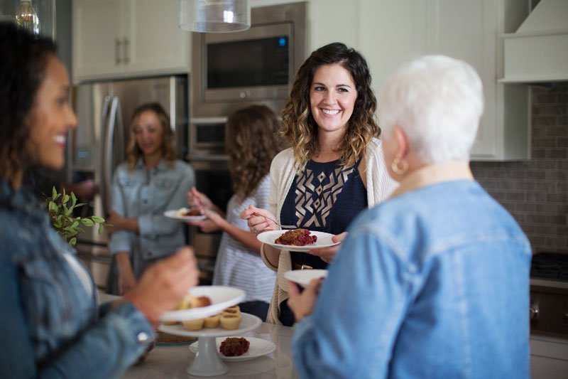 Women gathered around in kitchen eating desserts