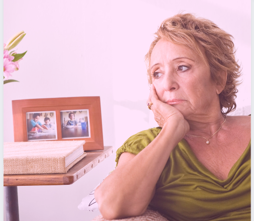 older woman with blonde hair, green shirt, sitting on couch with head in hand looking discouraged.